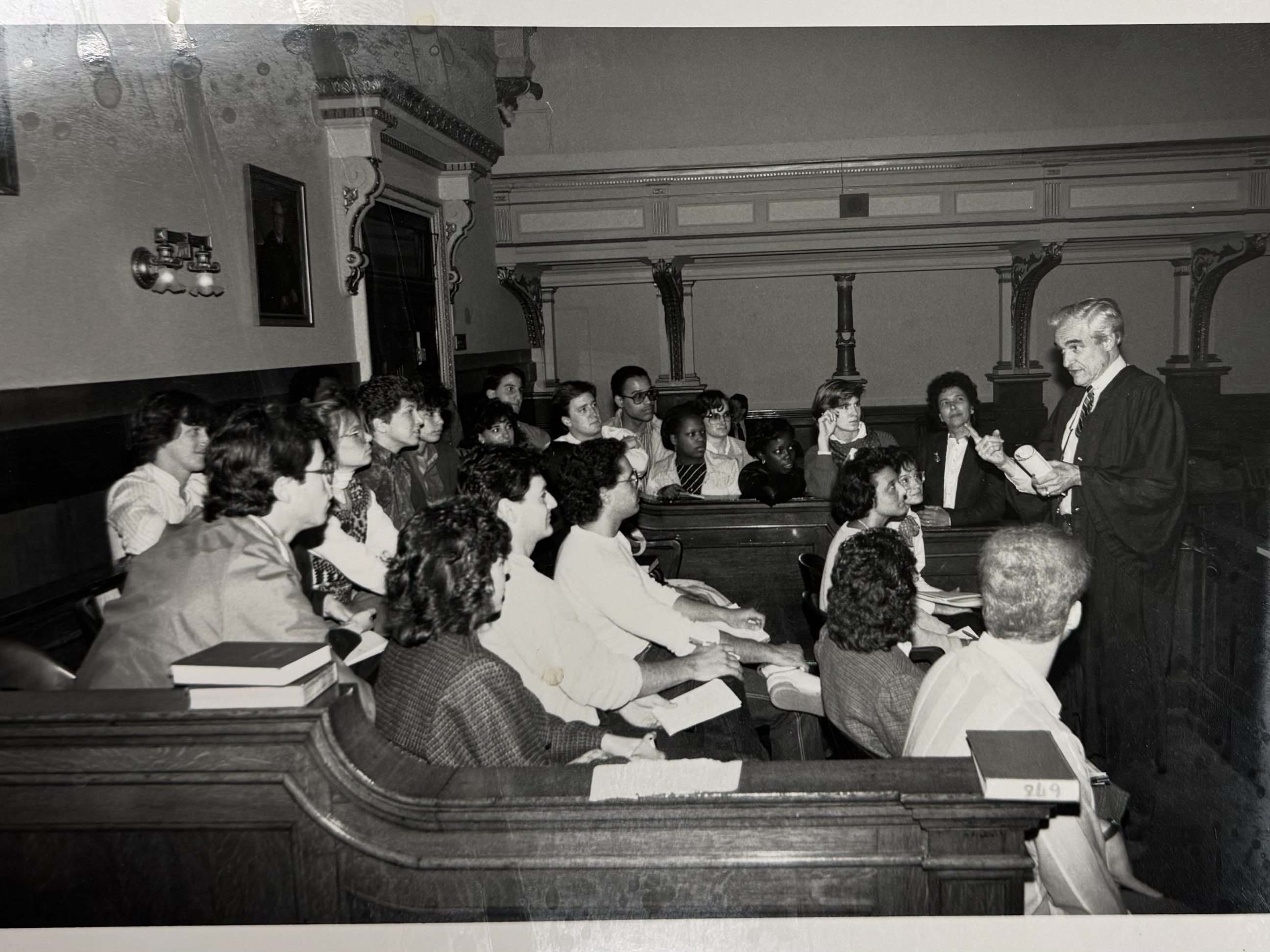 Black and white photograph of Dr. Julia Hall standing just to the left of a judge addressing a group of students in a courtroom. Date unknown.